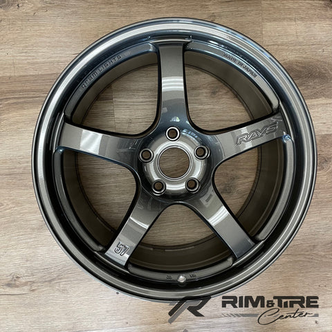 Photograph of a RAYS Gram Lights 57 five-spoke dark metallic gray car wheel with 'Made in Japan' marking, displayed on a light wooden floor with a 'Rim & Tire Center' logo in the bottom right corner