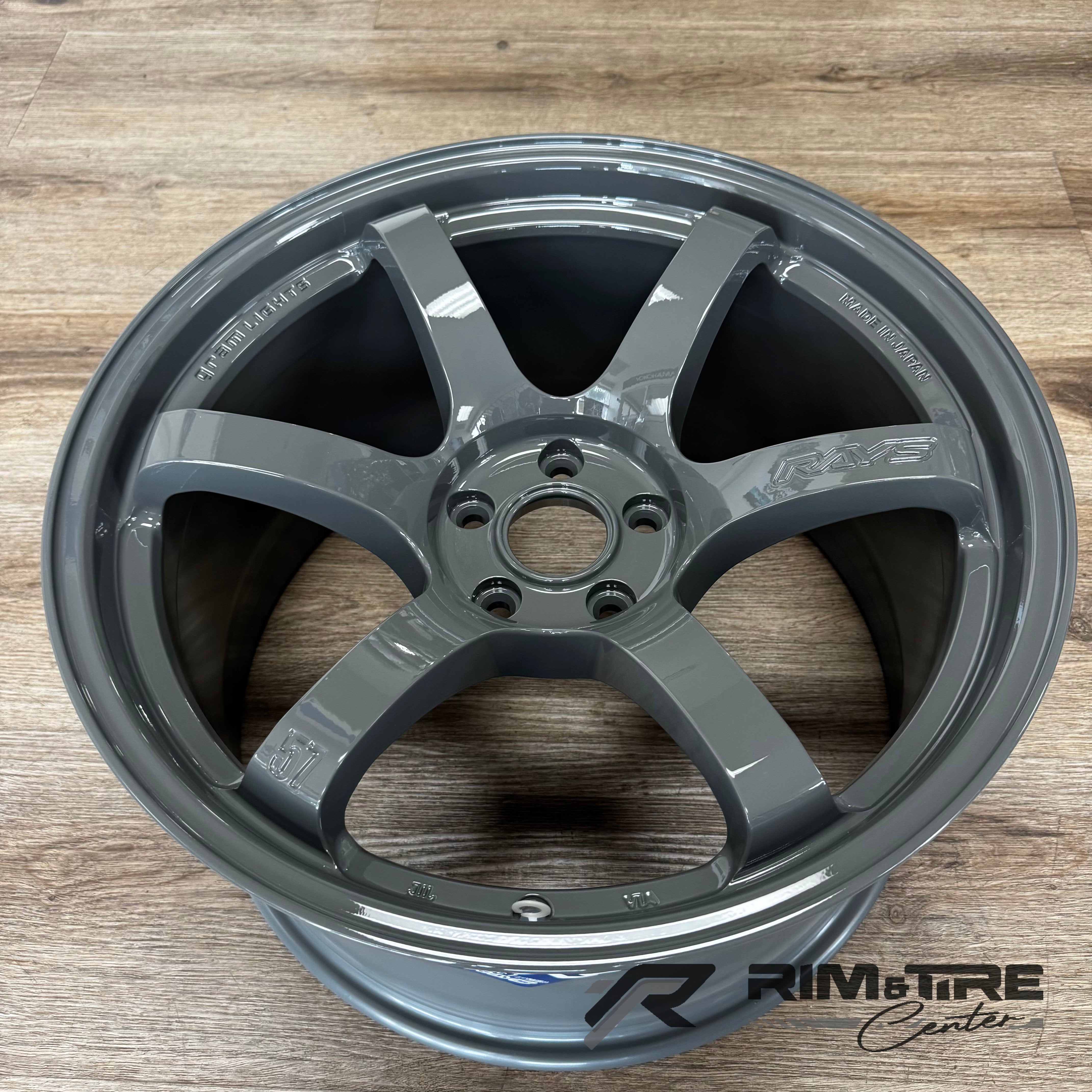 A RAYS Gram Lights glossy gray six-spoke car wheel with a high-gloss finish and "Made in Japan" and "57" markings displayed on a light brown wooden floor