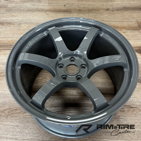 A RAYS Gram Lights glossy gray six-spoke car wheel with a high-gloss finish and "Made in Japan" and "57" markings displayed on a light brown wooden floor