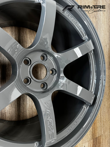 Product photograph of a glossy light grey RAYS Gram Lights five-spoke automotive rim with MADE IN JAPAN inscription resting on a light brown wooden floor at a RIM & TIRE Center