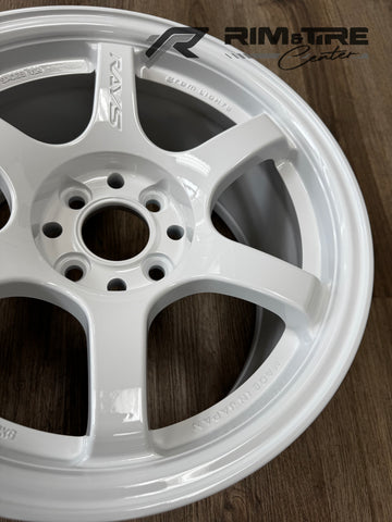 RAYS alloy wheel, a glossy white Gram Lights automotive rim with RAYS and GRAM LIGHTS branding, MADE IN JAPAN inscription, displayed on a wooden floor with the Rim & Tire Center logo
