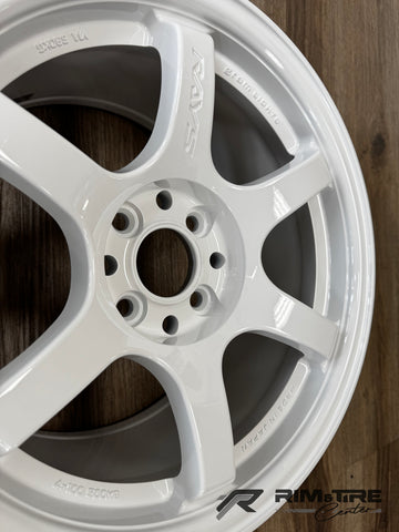 Photograph of a RAYS Gram Lights six-spoke car wheel in glossy white, showcasing Made In Japan and 4-100 500kg details against a wooden floor