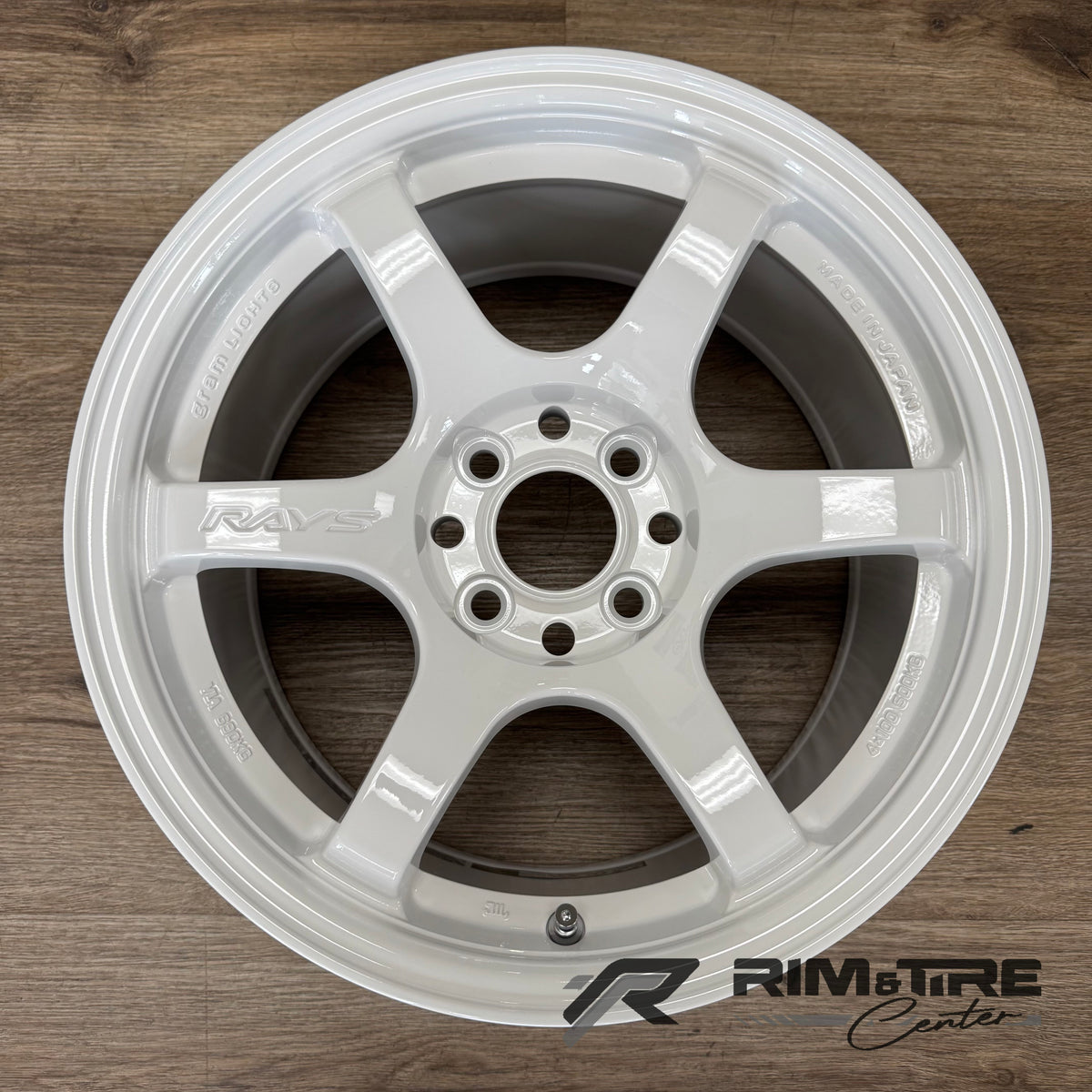 RAYS gram Lights car wheel, a modern gloss white six-spoke alloy, with prominent RAYS branding and "Made in Japan" engraving, presented on a warm wooden floor