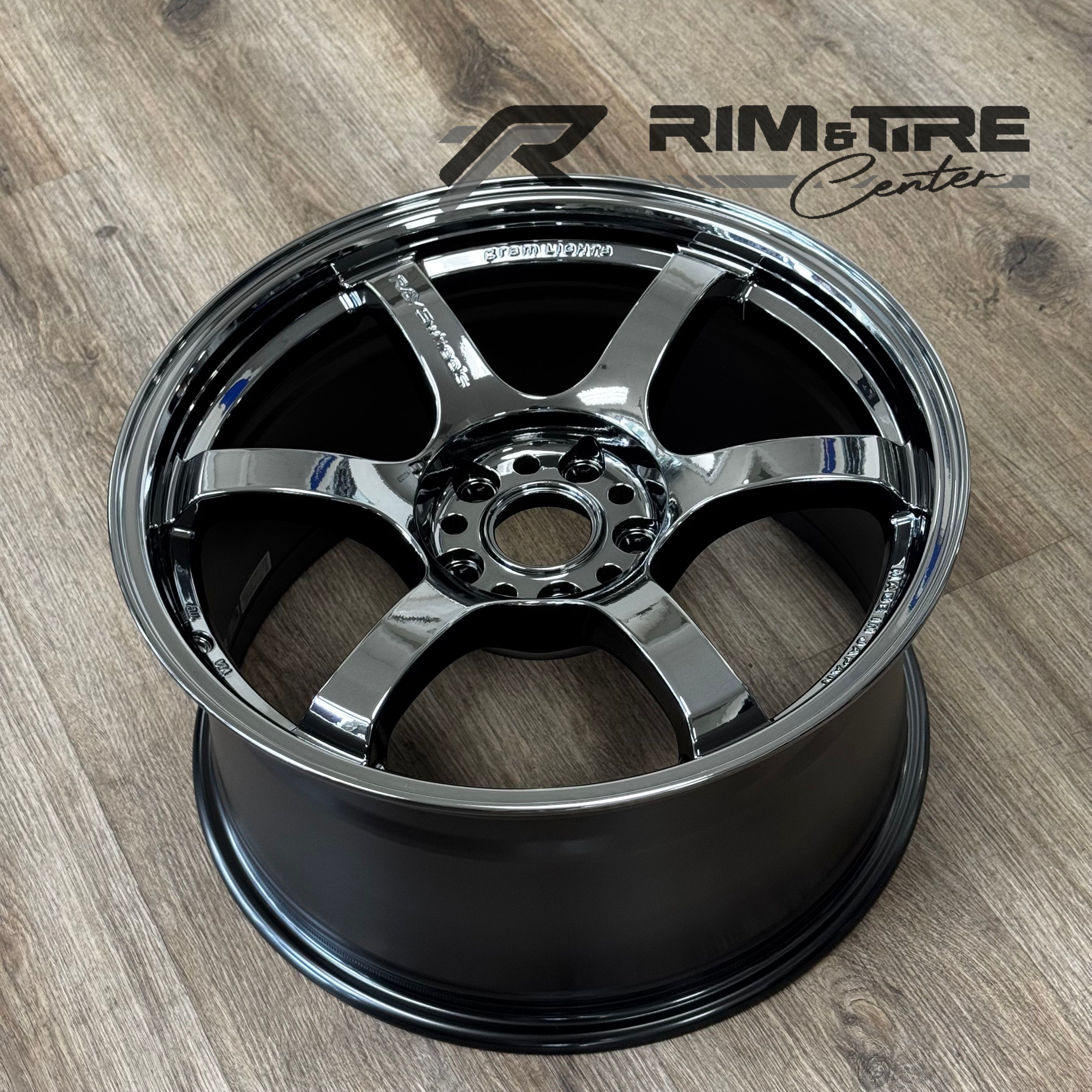 Photograph of a shiny chrome RAYS VOLK RACING Gram Lights six-spoke car wheel rim with a deep matte black inner barrel resting on a light brown wooden floor and showing "MADE IN JAPAN" engraving
