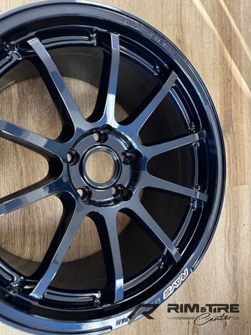 Photograph of a dark metallic blue RAYS Gram Lights multi-spoke alloy wheel with glossy finish, showing Made in Japan text on a wooden floor with a Rim & Tire Center watermark