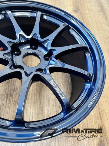 Forged aluminum Volk Racing RAYS ENG wheel, a close-up showing its glossy metallic blue finish, intricate ten-spoke design, and FORGED branding on a wooden surface