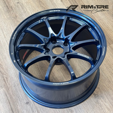 Photograph of a RAYS Engineering Volk Racing G025 M-SPEC forged car wheel in a glossy deep metallic blue finish with a ten-spoke design featuring 'Made in Japan' text, displayed on a light wooden floor