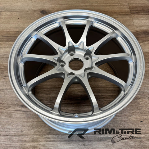 Photograph of a single matte silver Volk Racing M-Spec forged multi-spoke car wheel with "MADE IN JAPAN" engraving resting on a natural wooden floor