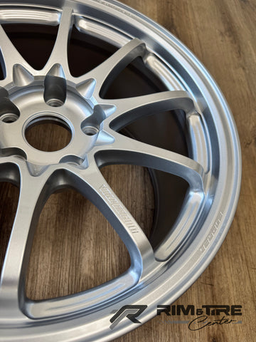 A silver multi-spoke Volk Racing forged car wheel displayed on a warm wooden floor