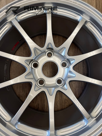Digital photograph of a silver matte metallic Volk Racing 10-spoke alloy wheel showcasing a five-lug bolt pattern and a prominent red inner rim sticker