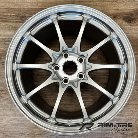 Product photo by Rim & Tire Center of a shiny silver 10-spoke Volk Racing forged car wheel Made in Japan displayed on a textured wooden floor