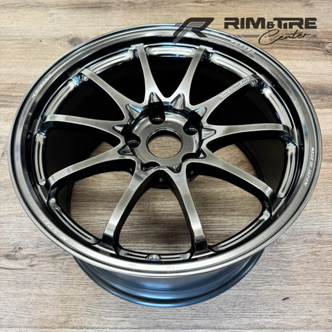 Digital photograph by RIM & TIRE Center showing a RAYS Volk Racing M-Spec forged alloy wheel with a dark chrome finish and intricate multi-spoke pattern featuring VOLK RACING and MADE IN JAPAN branding on a light wood floor