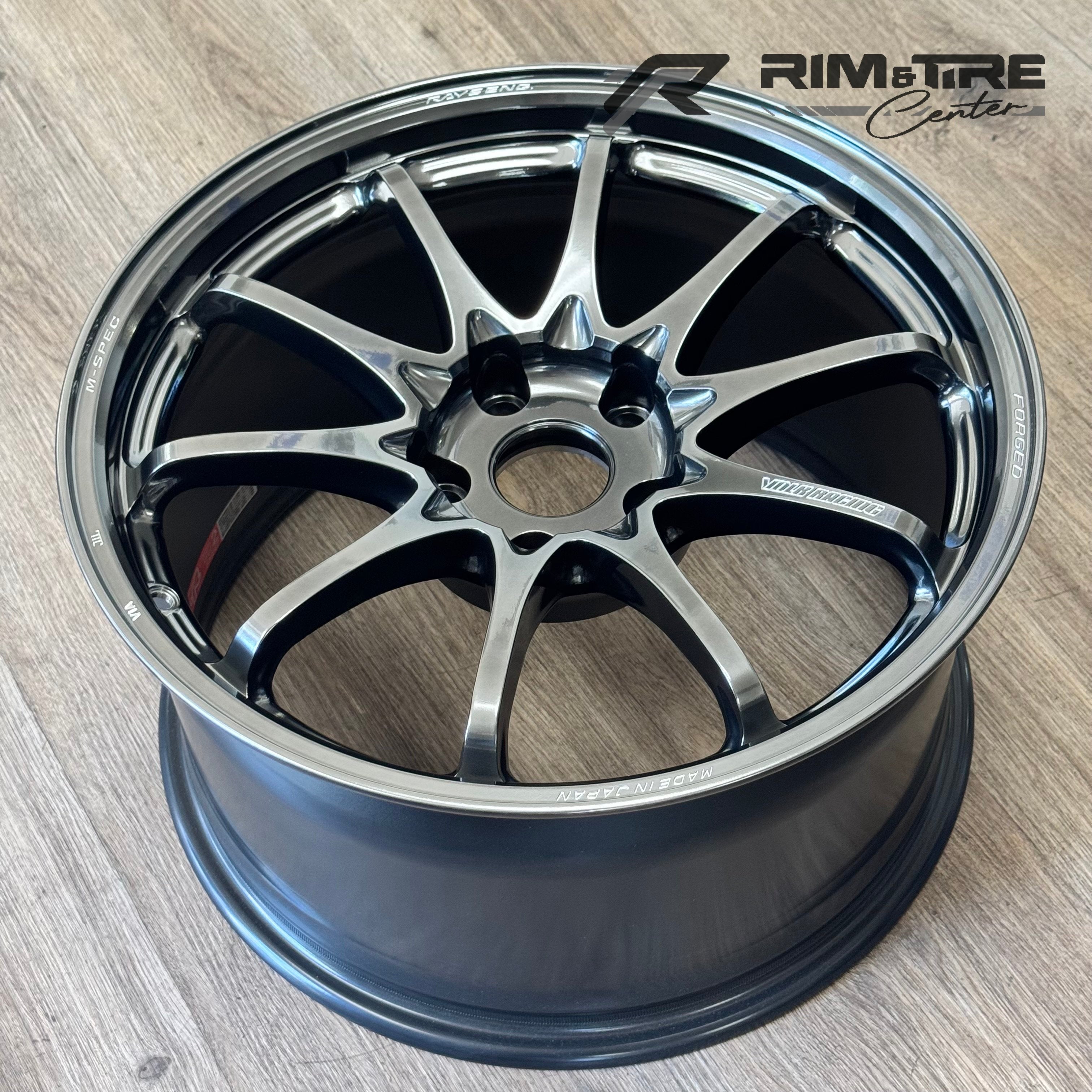 Photograph by RAYS VOLK RACING of a G025 forged alloy wheel on a light wood floor showcasing its glossy black and machined silver ten-spoke design with "FORGED" and "MADE IN JAPAN" text