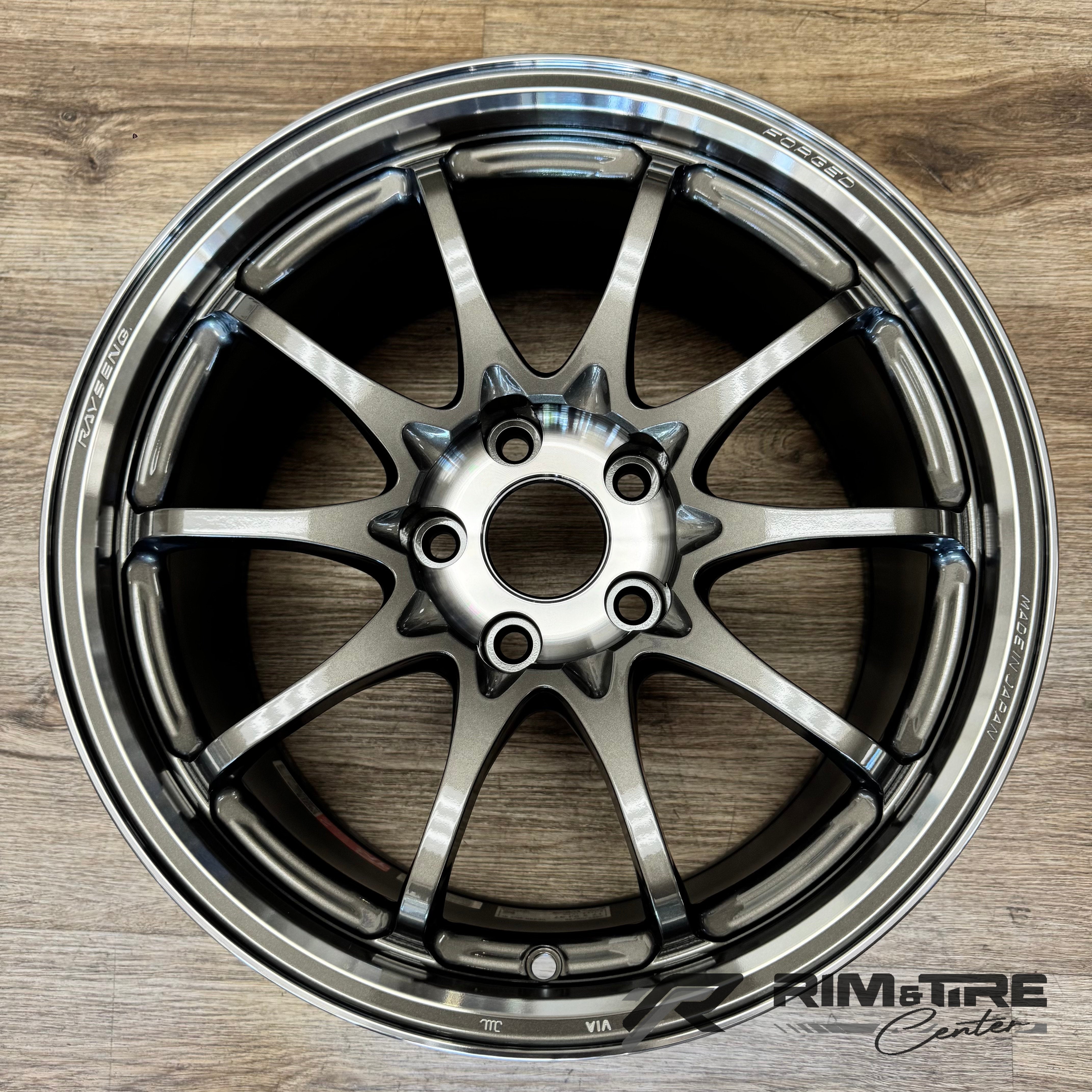 Photograph of a Rays Engineering forged gunmetal 10-spoke car wheel featuring a polished lip and 'RAYS ENG MADE IN JAPAN' branding, resting on a light wood floor