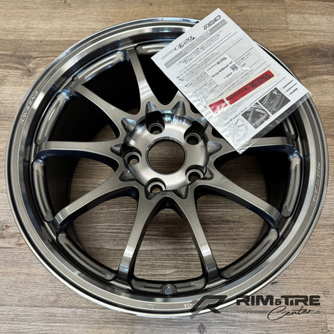 Photograph of a RAYS Engineering Volk Racing CE28N-plus SL 10-spoke alloy wheel in dark metallic grey on a light wood floor, featuring "RAYS ENG." and "MADE IN JAPAN" etched details and an accompanying RAYS sticker installation guide