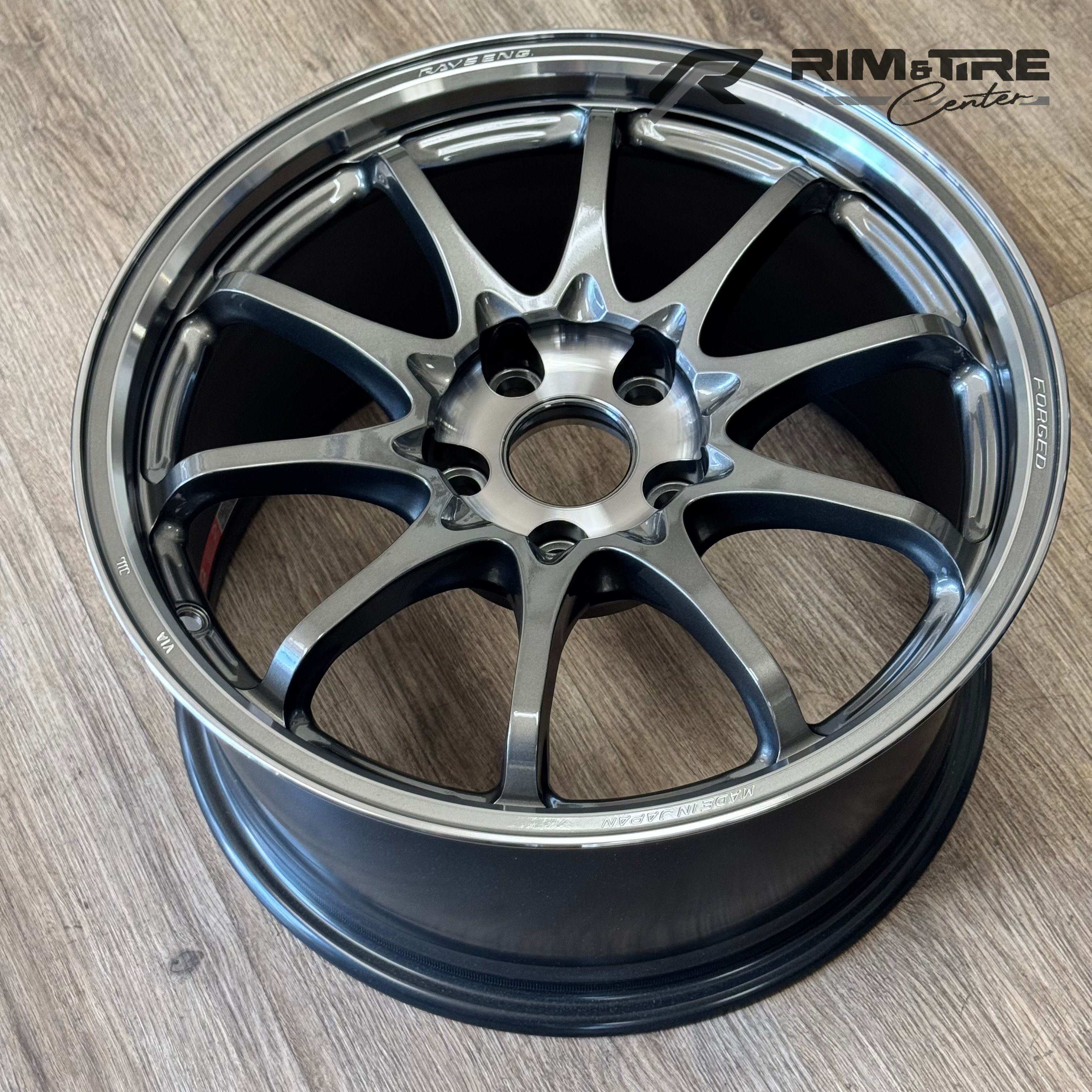 Photograph of a RAYS ENG multi-spoke forged car wheel in metallic grey with a polished lip on a wooden floor featuring a Rim & Tire Center watermark