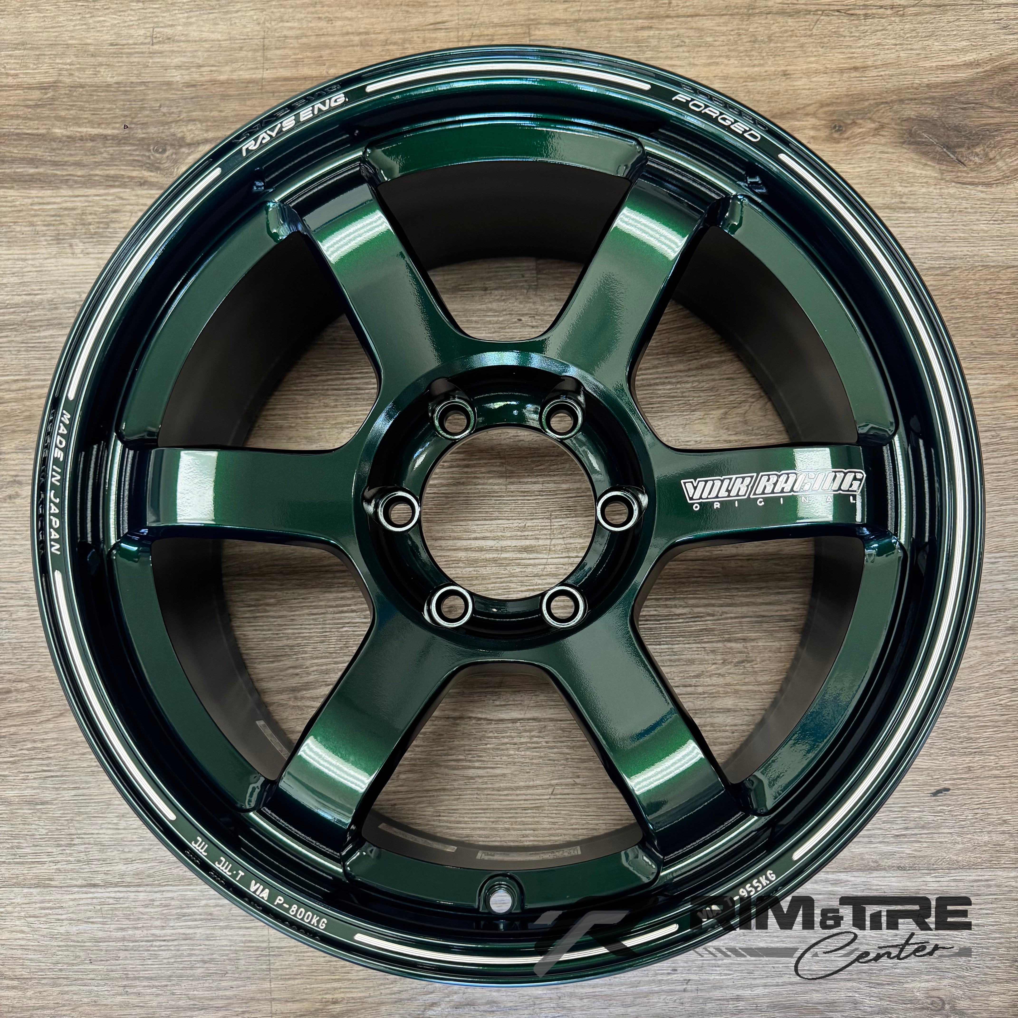 Forged RAYS Engineering Volk Racing wheel, a single deep glossy green six-spoke car rim, resting on a light brown wooden floor with distinctive "FORGED" and "MADE IN JAPAN" engravings and a bold silver "VOLK RACING" logo