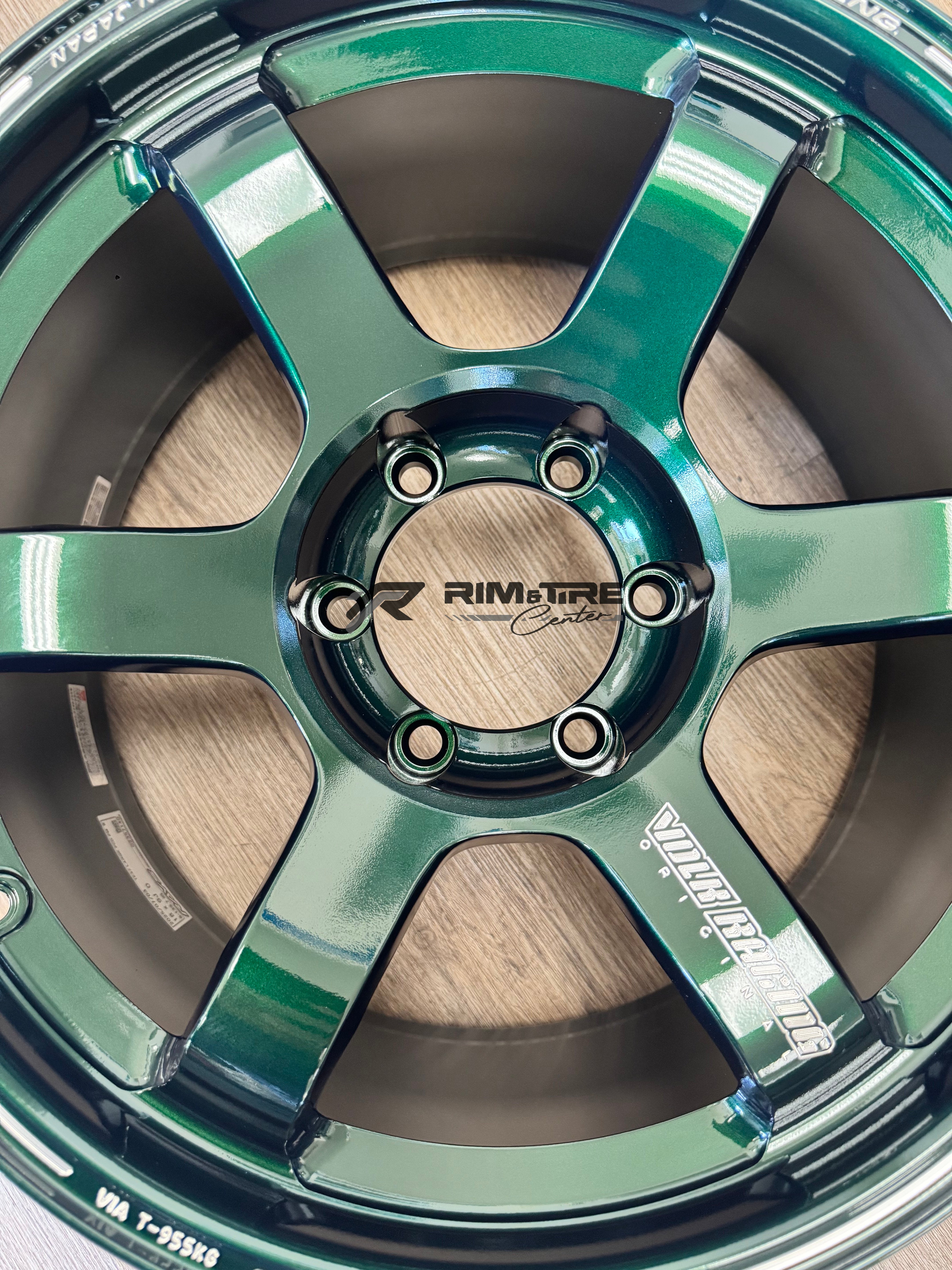 RAYS VOLK RACING forged aluminum wheel in metallic emerald green featuring a six-spoke design and 'VOLK RACING' branding, displayed on a wooden floor with the 'Rim & Tire Center' logo