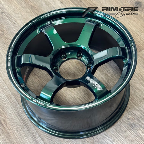 RAYS Volk Racing forged aluminum wheel in a striking glossy metallic green six-spoke design resting on a wooden floor with white FORGED and MADE IN JAPAN branding