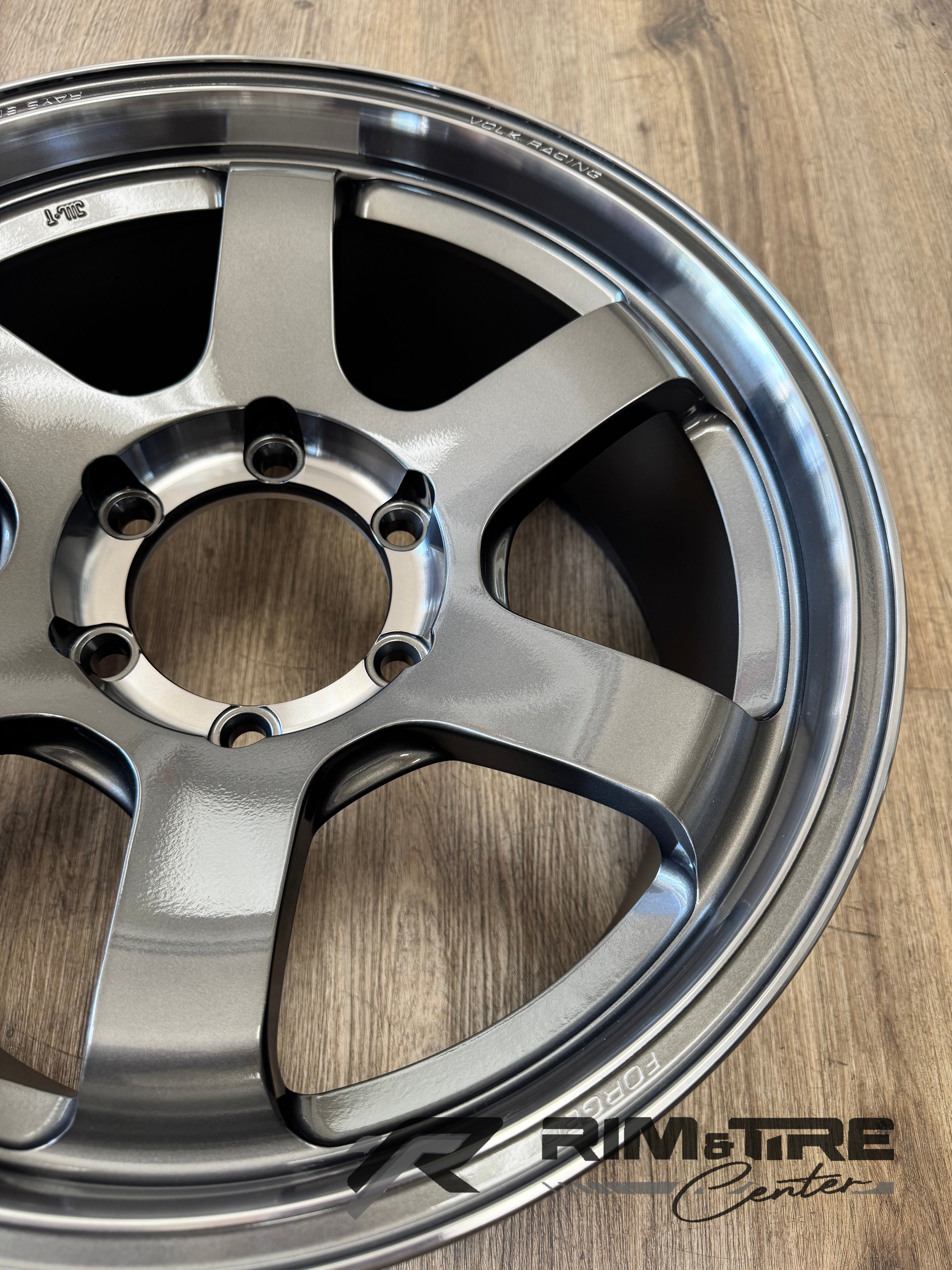 Product photo of a glossy silver Volk Racing TE37 six-spoke wheel resting on a wooden surface with embossed Rays Engineering and Volk Racing text