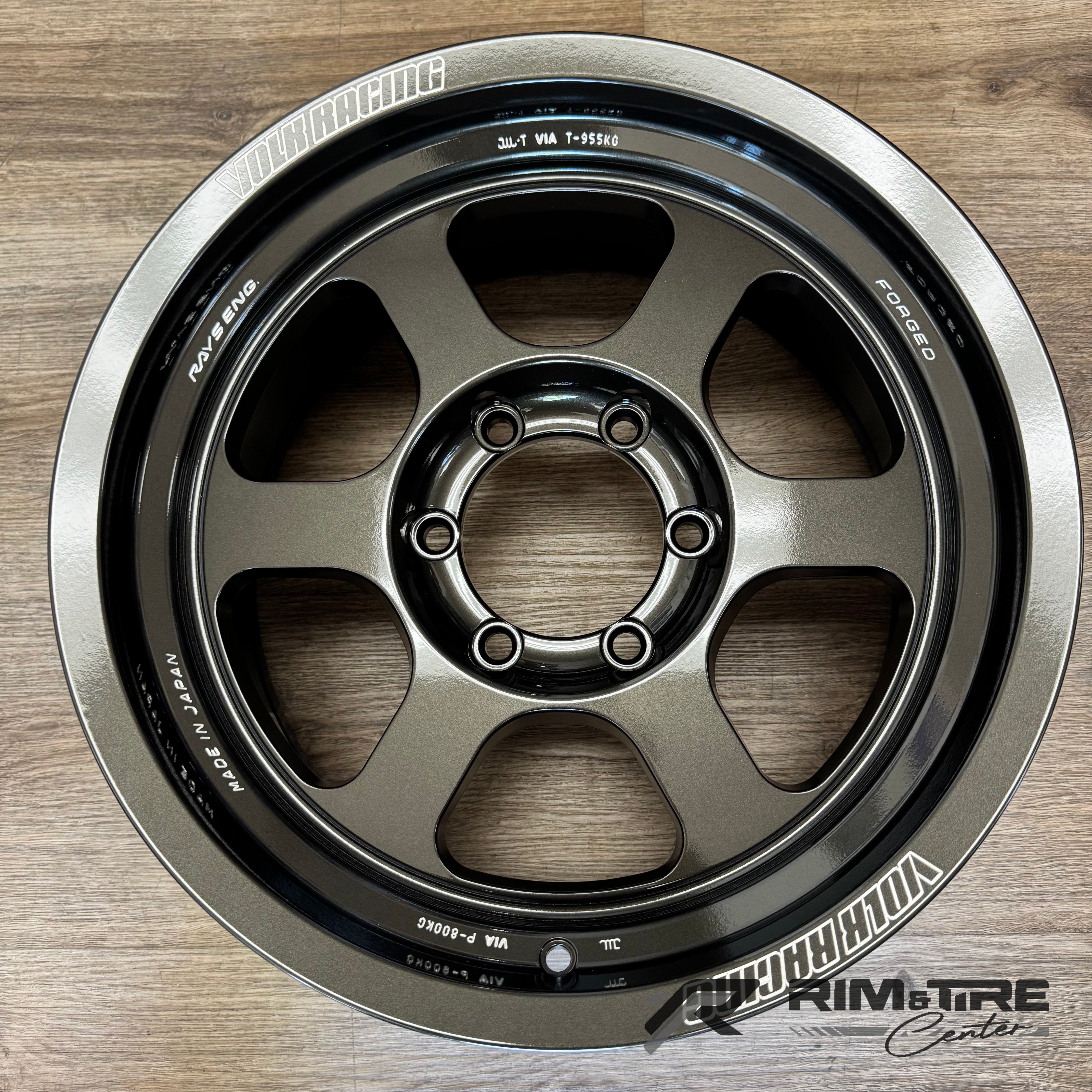 Volk Racing Rays Engineering forged aluminum wheel a single six-spoke design in dark metallic grey on a light wooden background featuring prominent white VOLK RACING and RAYS ENG branding a contrasting polished silver outer edge and visible MADE IN JAPAN text