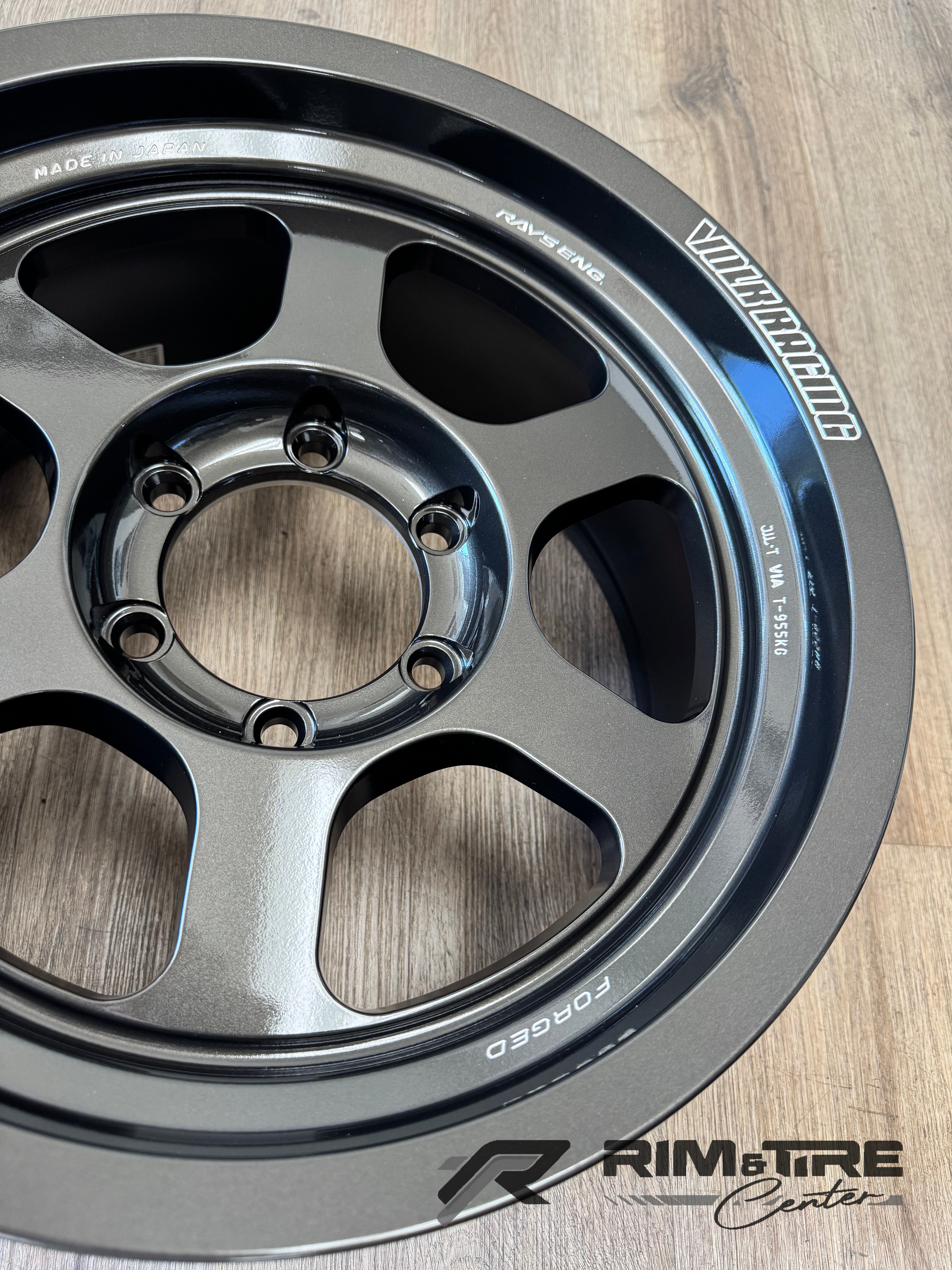 Photograph of a dark gray RAYS VOLK RACING TE37 forged rim proudly displaying MADE IN JAPAN and RAYS ENG etching on its surface resting on a wooden floor