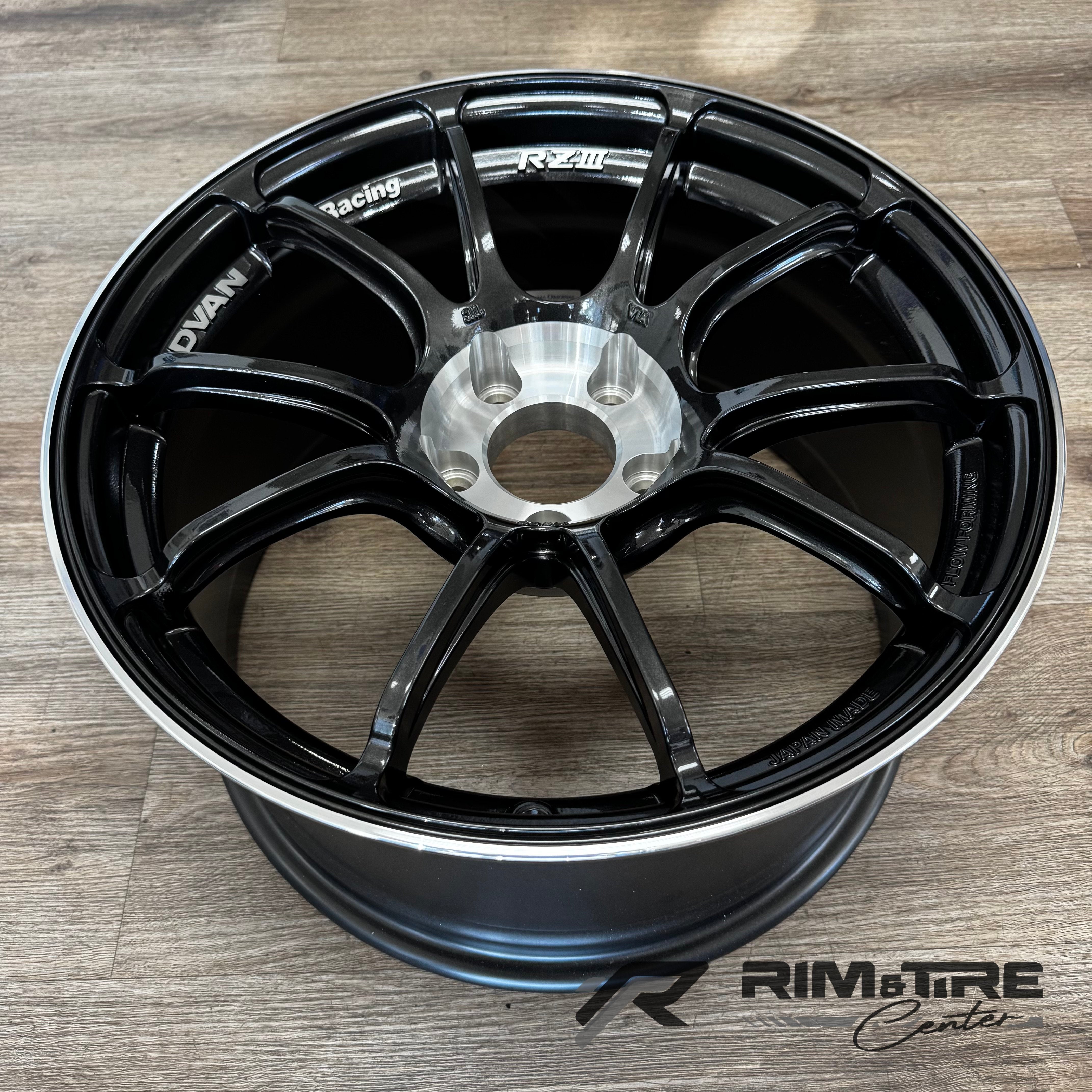 ADVAN Racing RZII glossy black multi-spoke car wheel with a silver machined center hub and outer lip, featuring "JAPAN MADE" text, photographed on a light wooden floor