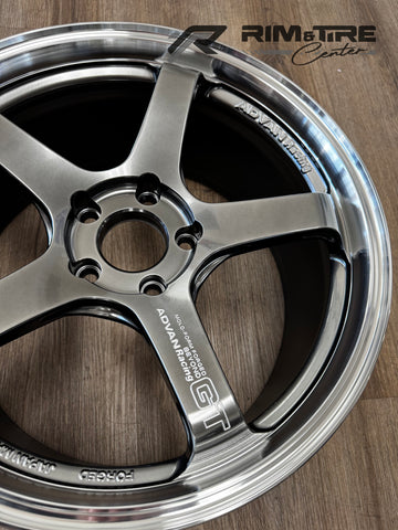 Product photograph of an Advan Racing GT forged five-spoke automotive wheel in a glossy gunmetal finish, featuring 'MOLD-FORM FORGED BEYOND' and 'JAPAN MADE' text, displayed on a light wooden floor with the Rim & Tire Center watermark