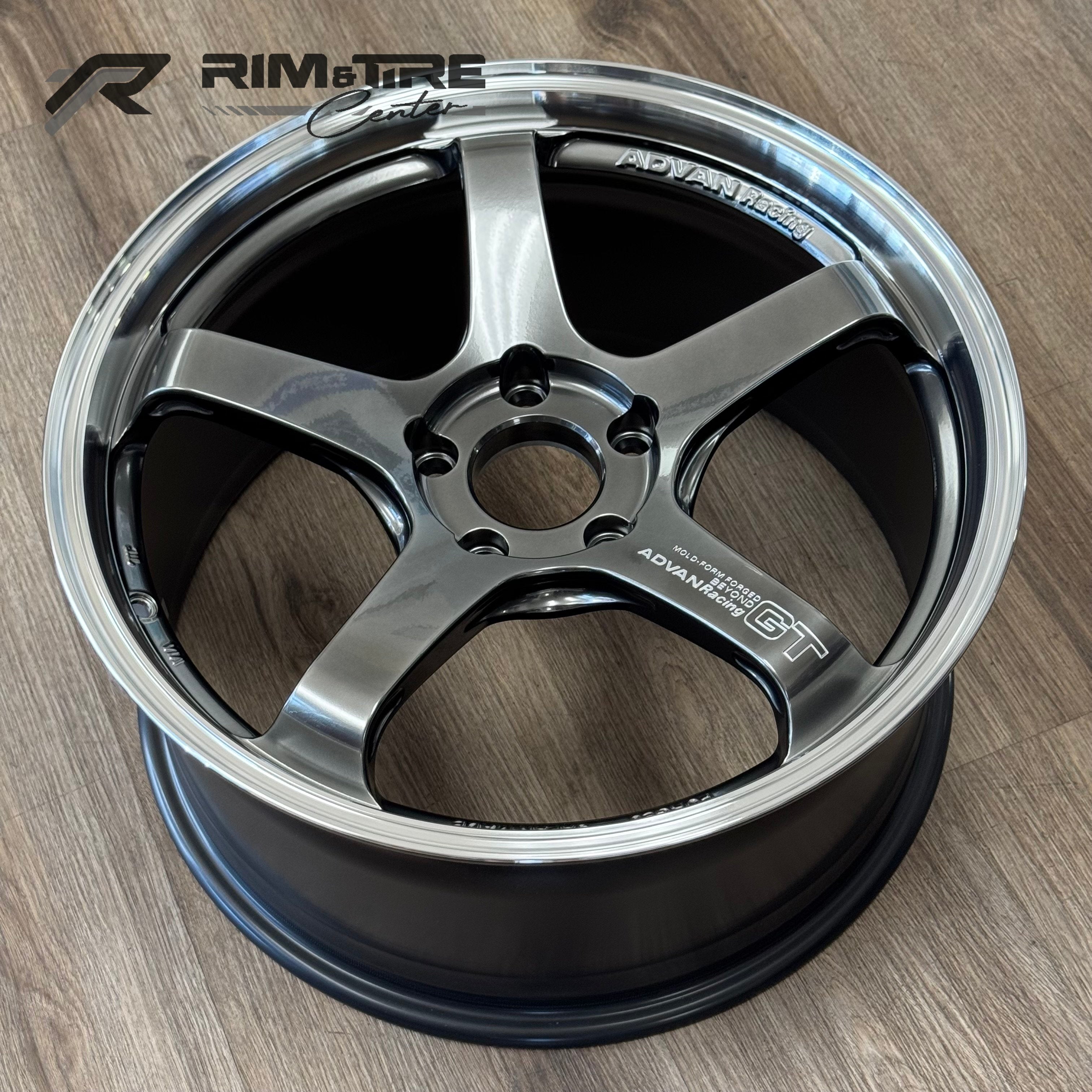 ADVAN Racing GT forged alloy wheel in dark metallic gray with a five-spoke design and polished silver lip resting on a light wood grain floor
