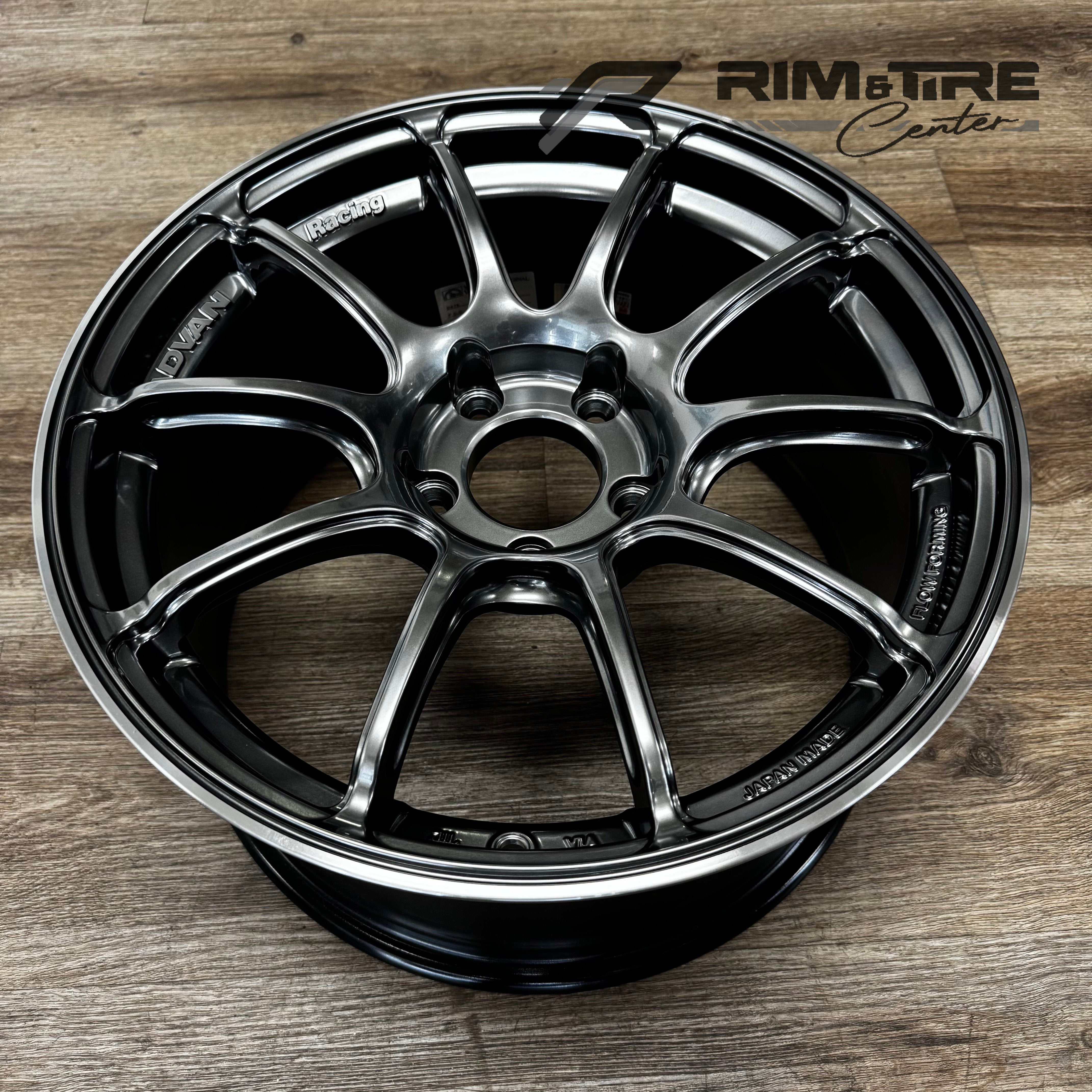 Digital photograph of a Yokohama Advan Racing 10-spoke car wheel featuring a dark metallic gray finish and polished silver lip on a wooden floor