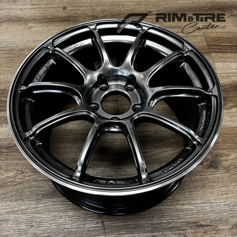 Digital photograph of a Yokohama Advan Racing 10-spoke car wheel featuring a dark metallic gray finish and polished silver lip on a wooden floor
